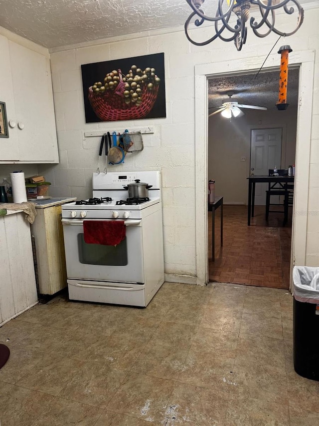 kitchen with light countertops, concrete block wall, white range with gas stovetop, a textured ceiling, and ceiling fan