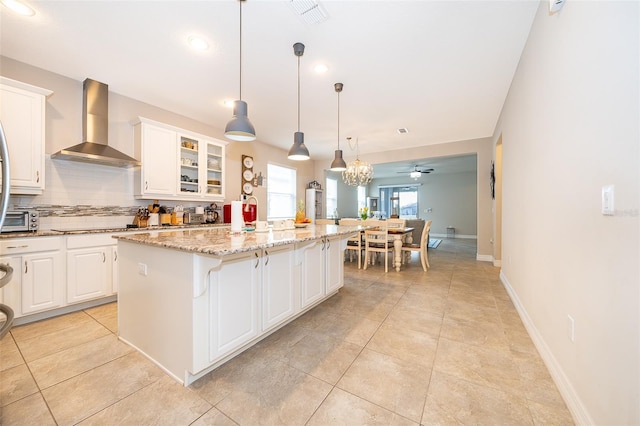 kitchen featuring backsplash, a kitchen island, light stone countertops, visible vents, and wall chimney exhaust hood