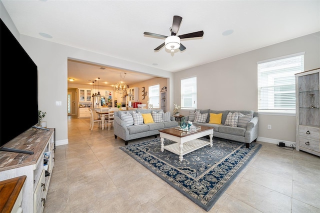 living area with light tile patterned floors, ceiling fan with notable chandelier, and baseboards