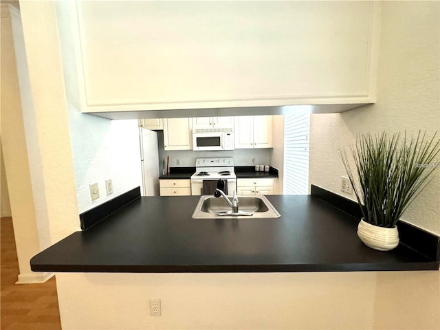 kitchen featuring white cabinets, a sink, dark countertops, white appliances, and a peninsula