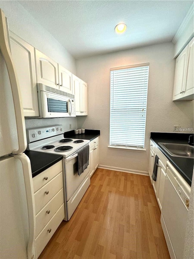 kitchen with white cabinets, white appliances, a sink, and dark countertops