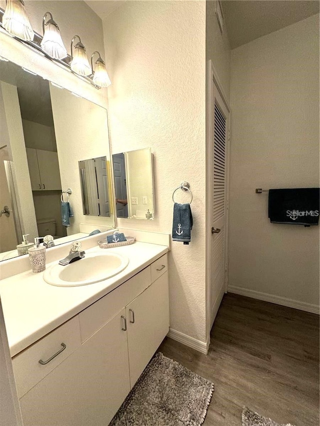 bathroom with a textured wall, baseboards, vanity, and wood finished floors