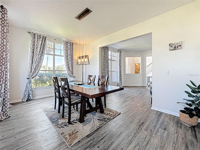 dining room featuring a notable chandelier, a textured ceiling, baseboards, and wood finished floors