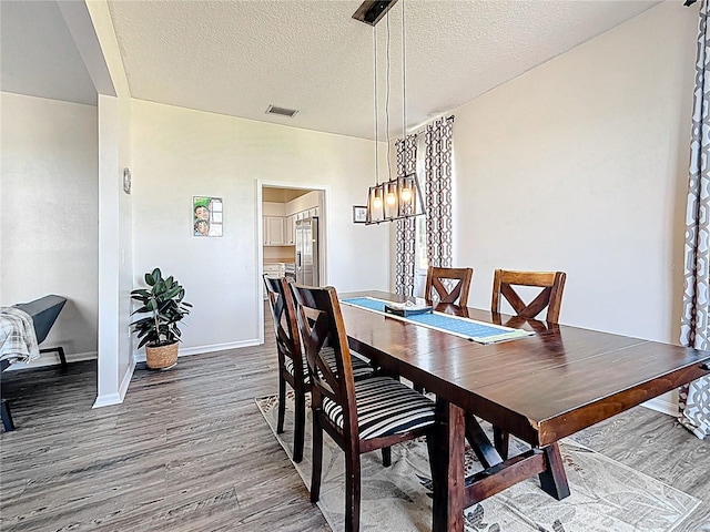 dining room with visible vents, baseboards, a chandelier, a textured ceiling, and wood finished floors