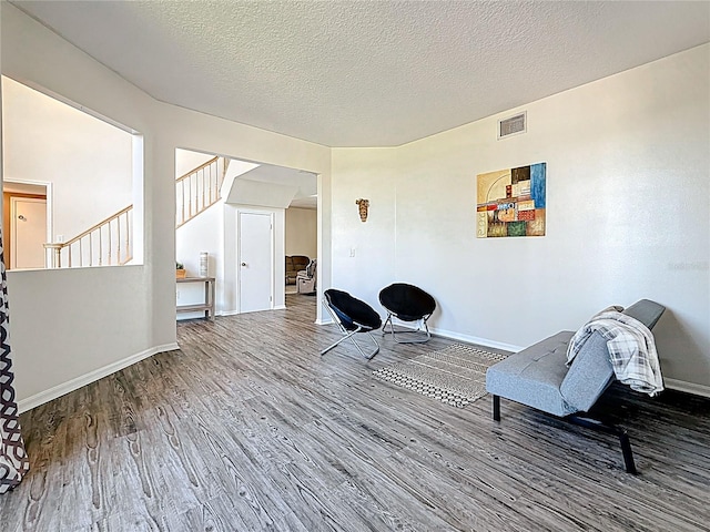 living area featuring baseboards, stairway, a textured ceiling, visible vents, and wood finished floors