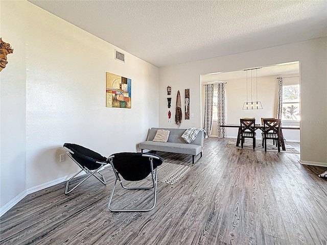 living area featuring visible vents, baseboards, wood finished floors, and a textured ceiling