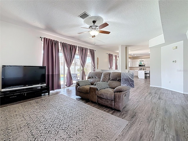 living area featuring visible vents, a textured ceiling, wood finished floors, and ceiling fan