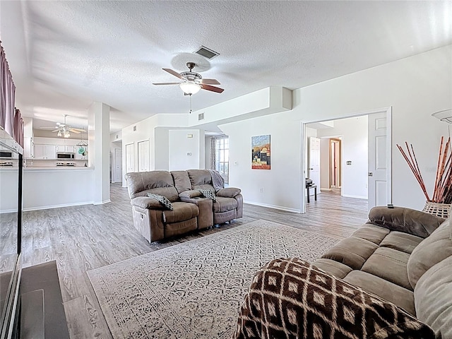 living area with ceiling fan, light wood-style flooring, a textured ceiling, visible vents, and baseboards