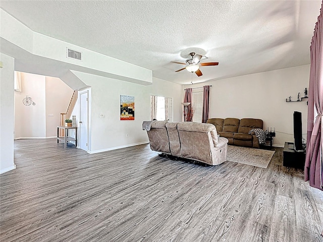 living area featuring baseboards, a textured ceiling, a ceiling fan, visible vents, and wood finished floors