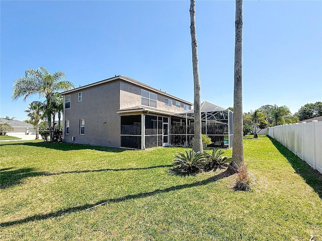 rear view of house with stucco siding, fence, and a lawn