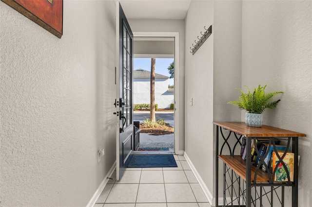 doorway to outside featuring baseboards, light tile patterned flooring, and a textured wall