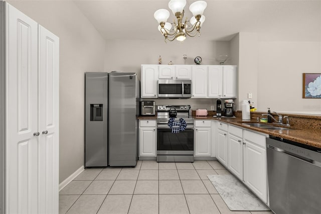 kitchen with stainless steel appliances, dark countertops, a sink, white cabinetry, and a notable chandelier