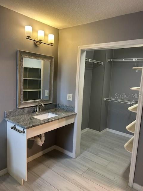 bathroom featuring baseboards, a sink, a textured ceiling, and wood finished floors
