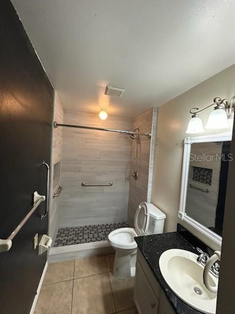 full bathroom with toilet, a tile shower, tile patterned floors, visible vents, and vanity