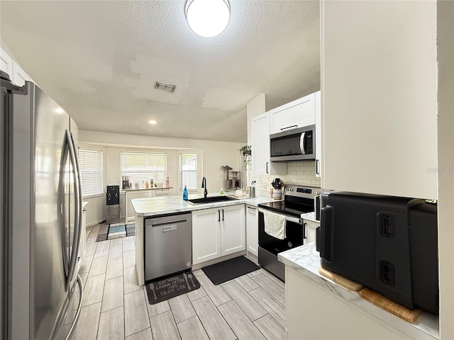 6922 Doehring Dr, Lakeland, FL 33810 - kitchen with appliances with stainless steel finishes, a sink, a peninsula, white cabinetry, and visible vents