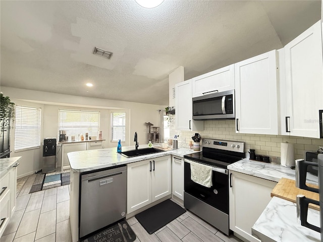 6922 Doehring Dr, Lakeland, FL 33810 - kitchen with white cabinets, a sink, stainless steel appliances, a peninsula, and visible vents