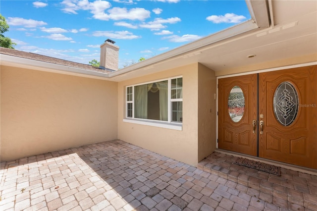 doorway to property with a patio area, stucco siding, and a chimney