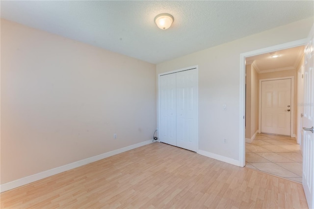 unfurnished bedroom featuring a closet, light wood-type flooring, baseboards, and ornamental molding
