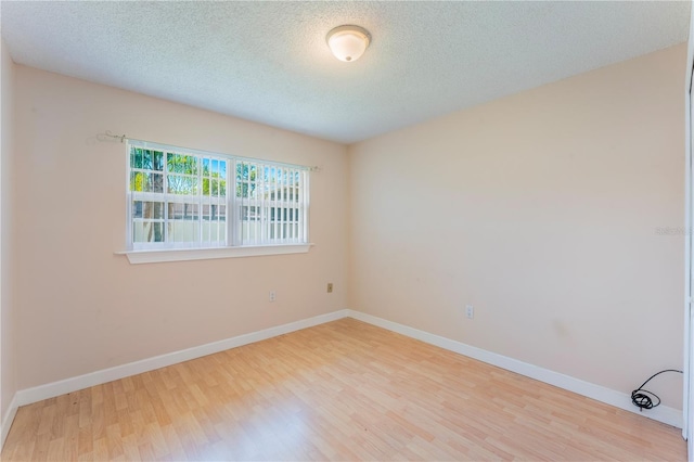 spare room with a textured ceiling, baseboards, and wood finished floors