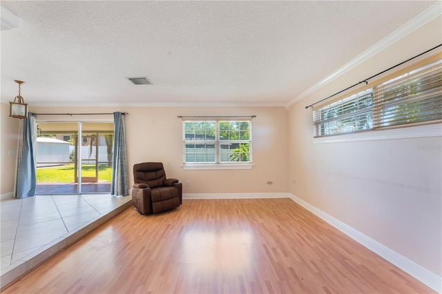 unfurnished room featuring a textured ceiling, wood finished floors, baseboards, and ornamental molding