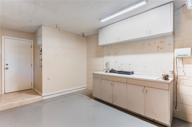 kitchen with baseboards, white cabinets, light countertops, a textured ceiling, and concrete flooring