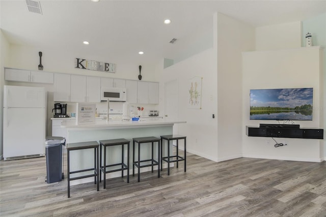 2237 Wyndham Palms Way, Kissimmee, FL 34747 - kitchen with white appliances, light wood-style flooring, white cabinets, visible vents, and a kitchen bar