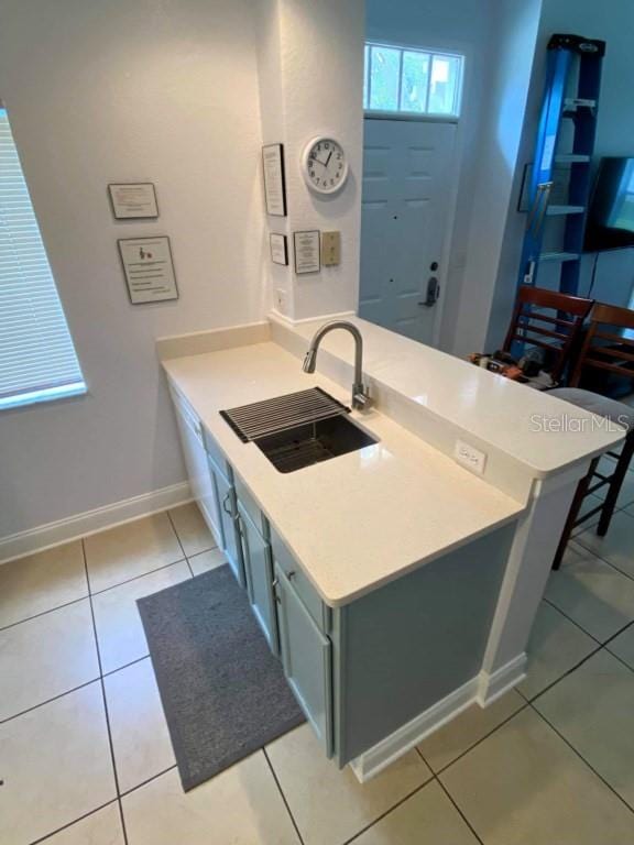 kitchen featuring light tile patterned floors, baseboards, a sink, light countertops, and a peninsula