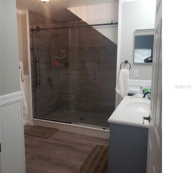 full bath featuring a shower stall, vanity, a wainscoted wall, and wood finished floors