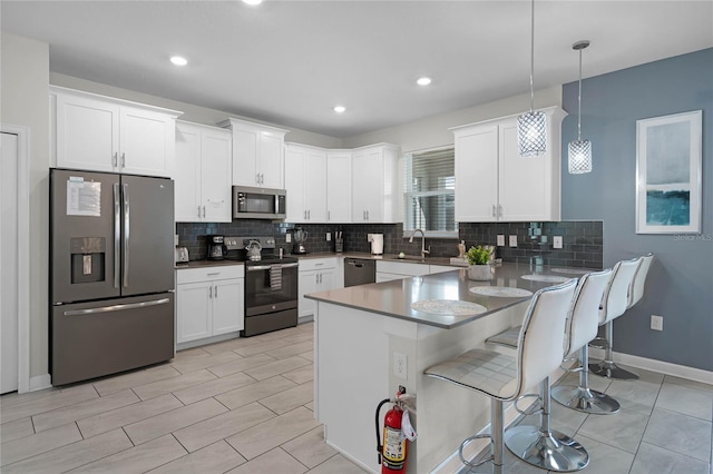 kitchen with a kitchen breakfast bar, a peninsula, white cabinets, appliances with stainless steel finishes, and decorative backsplash