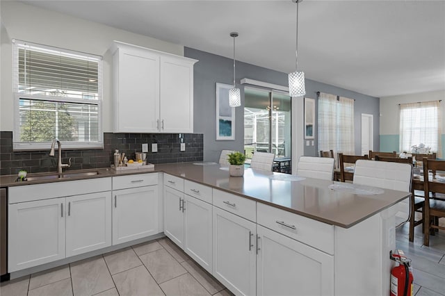 kitchen featuring a peninsula, white cabinets, decorative backsplash, a sink, and hanging light fixtures