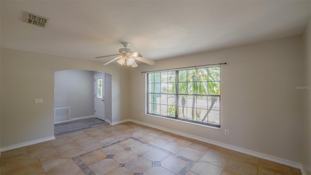 spare room featuring arched walkways, light tile patterned floors, visible vents, and a ceiling fan