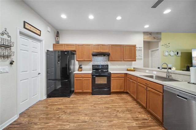 kitchen featuring visible vents, light countertops, a sink, light wood finished floors, and black appliances