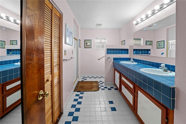 bathroom with a textured ceiling, a shower stall, a sink, and a closet