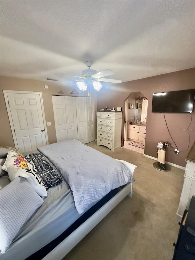 bedroom featuring ceiling fan, connected bathroom, a closet, light colored carpet, and baseboards