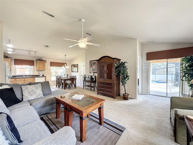 living area featuring vaulted ceiling, visible vents, light carpet, and ceiling fan with notable chandelier
