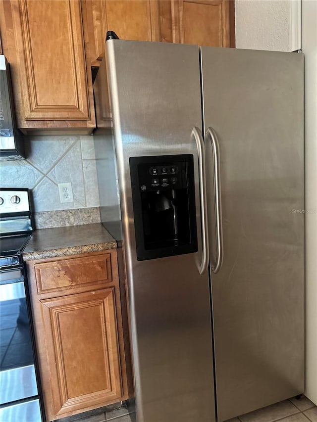 6141 Metrowest Blvd Unit 303, Orlando, FL 32835 - kitchen with stainless steel appliances, dark countertops, brown cabinetry, backsplash, and light tile patterned floors