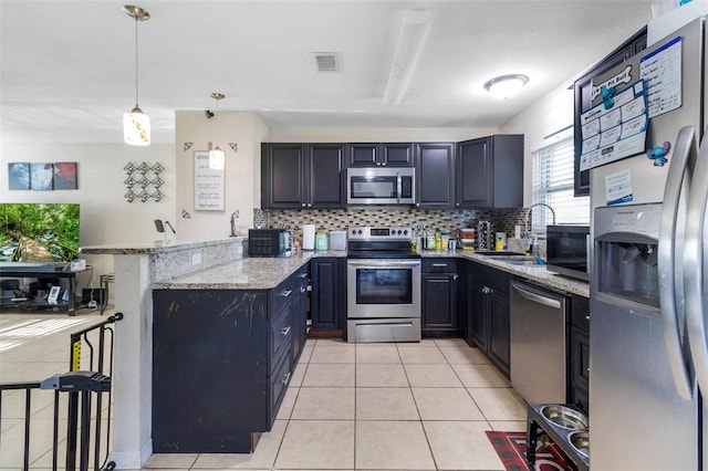 kitchen featuring appliances with stainless steel finishes, a peninsula, light tile patterned flooring, decorative backsplash, and a sink