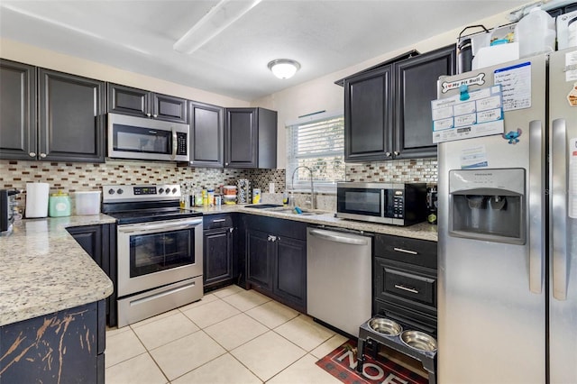 kitchen with dark cabinets, appliances with stainless steel finishes, light tile patterned floors, decorative backsplash, and a sink