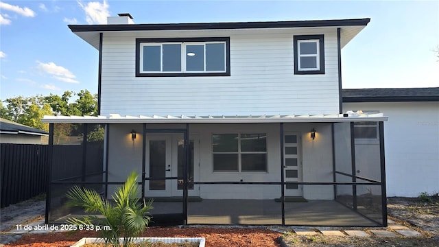 view of front of house with french doors, a chimney, metal roof, fence, and a sunroom