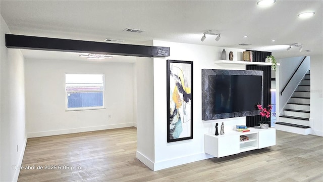 living room featuring light wood finished floors, baseboards, visible vents, and stairway