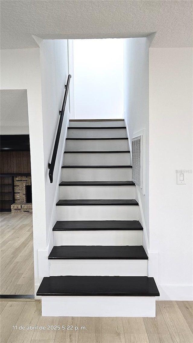 stairway featuring a textured ceiling, wood finished floors, visible vents, and a fireplace