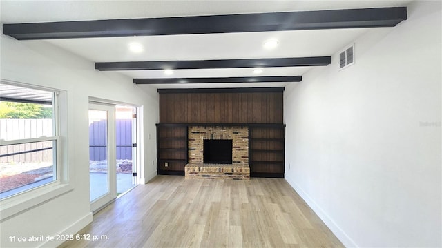 unfurnished living room with beamed ceiling, visible vents, light wood finished floors, and baseboards