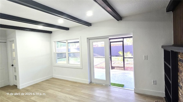 interior space featuring light wood-style flooring, baseboards, beam ceiling, and a brick fireplace