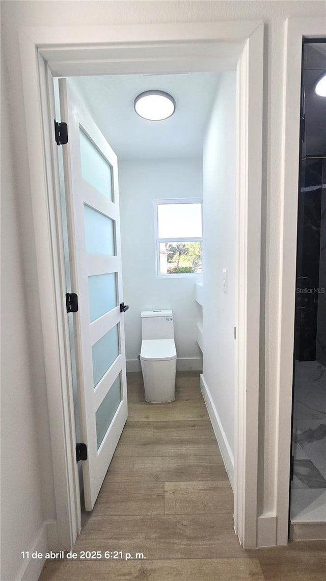 bathroom featuring baseboards, wood finished floors, and toilet