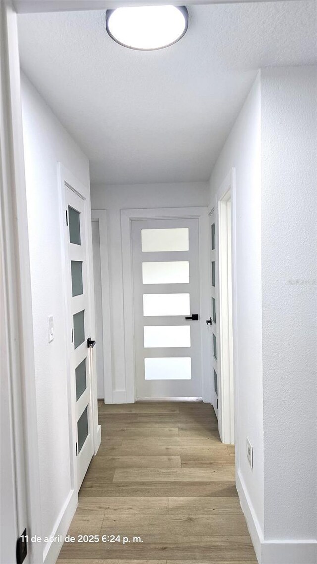 hallway featuring light wood-type flooring, baseboards, and a textured ceiling