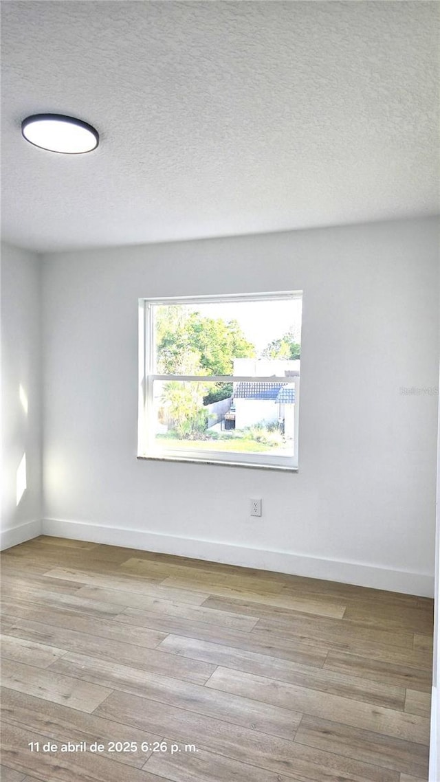 empty room featuring baseboards, a textured ceiling, and light wood-style flooring