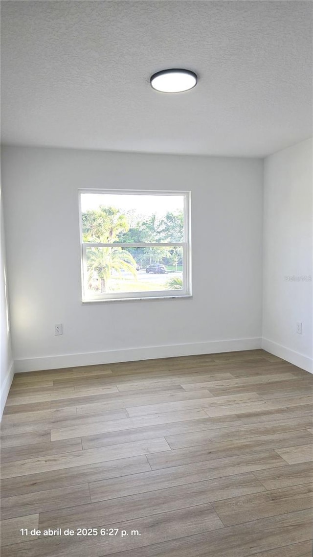 unfurnished room featuring baseboards, a textured ceiling, and light wood-type flooring