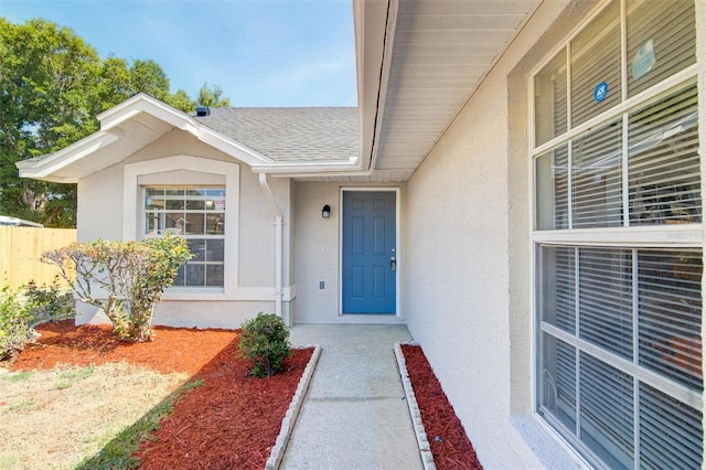 entrance to property with fence, a shingled roof, and stucco siding