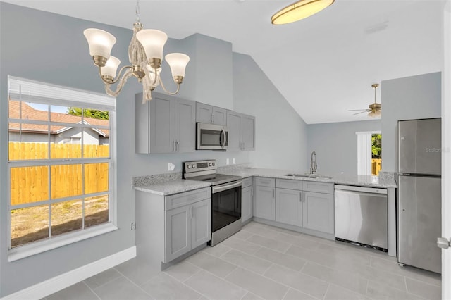 kitchen with a sink, a healthy amount of sunlight, lofted ceiling, appliances with stainless steel finishes, and gray cabinetry
