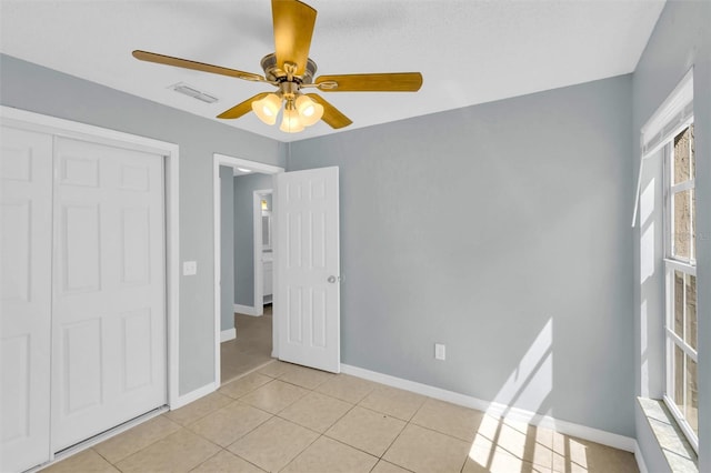 unfurnished bedroom featuring baseboards, visible vents, a closet, ceiling fan, and light tile patterned floors